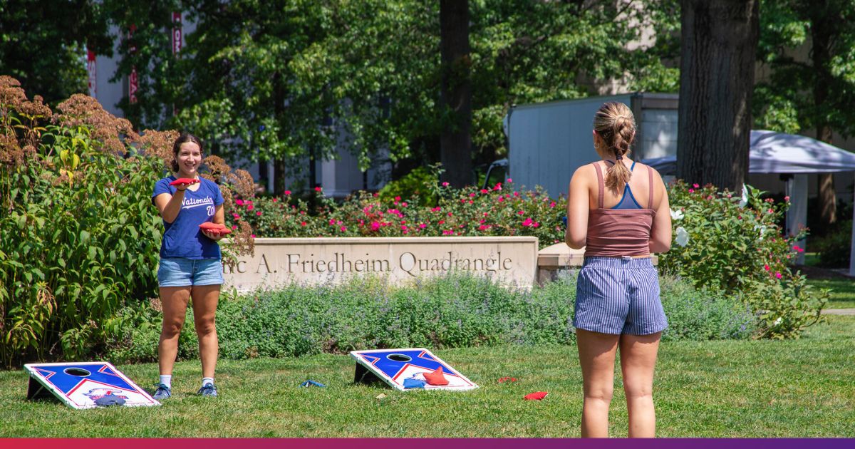 Two students playing cornhole on the Quad at American University.