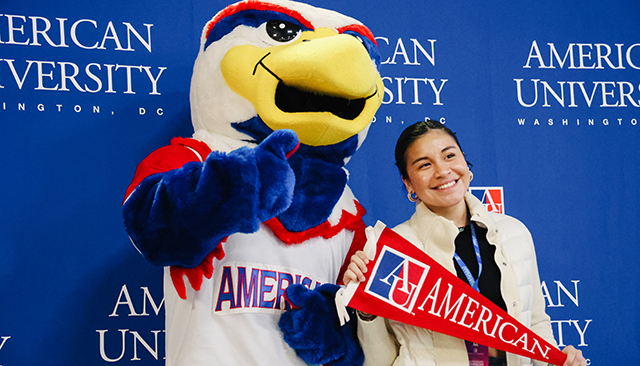 Image of student holding a pennant that says American with AU mascot Clawed Z. Eagle