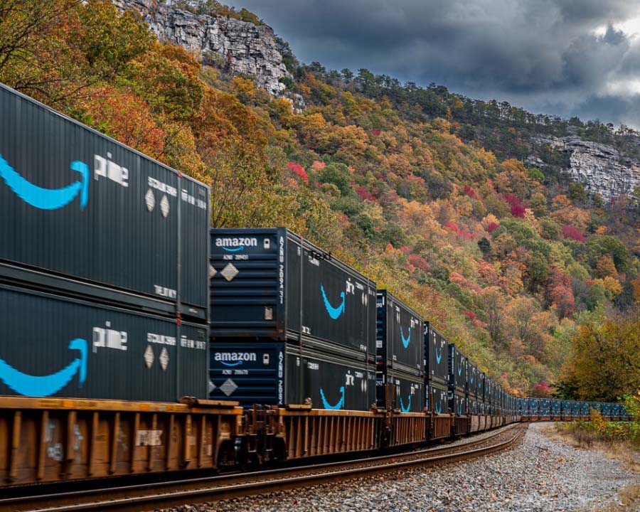 “American Prime” by Pedro Ledesma III. A freight train with Amazon shipping containers driving through wooded mountains. 