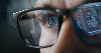 A man wearing eyeglasses with computer code reflected in one lens