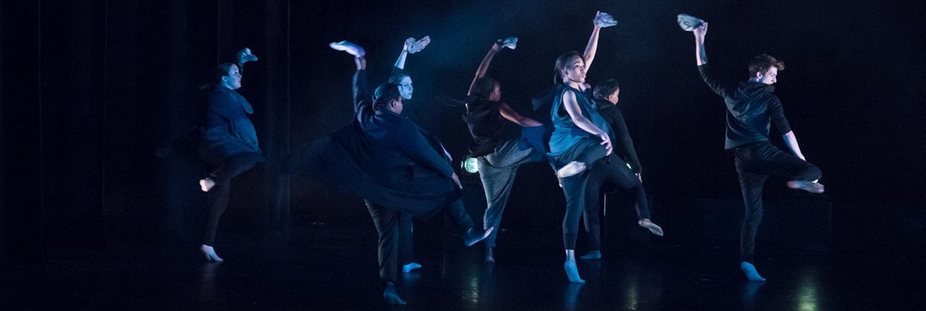 Dancer lit in blue each raise one leg and wave a kerchief