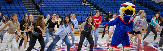 Clawed the eagle and students dancing on a basketball court