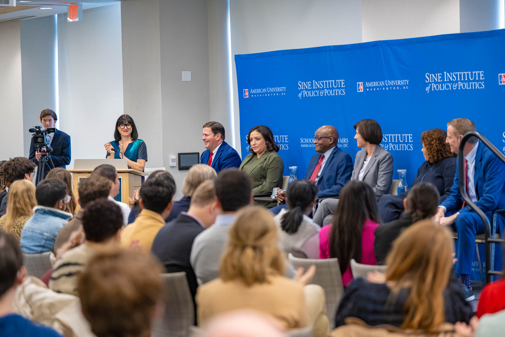 A crowd applauds a panel of speakers.