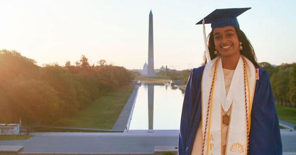 Dhanya Rao in her Commencement regalia at the Lincoln Memorial with the reflecting pool and Washington Monument in the background.