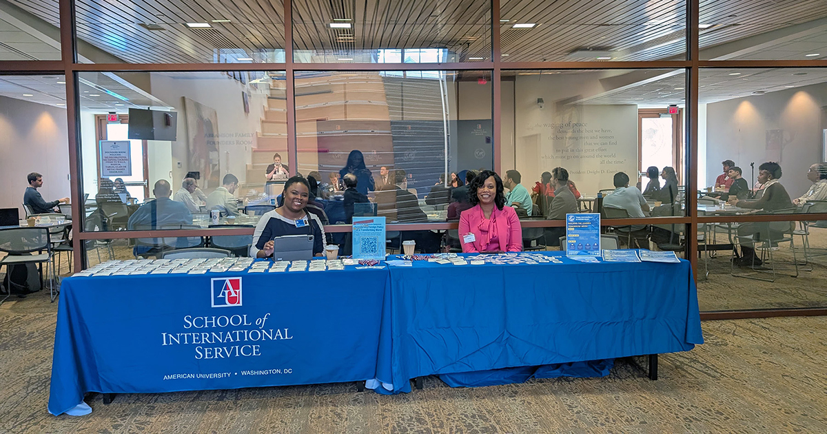 Two staff members sitting at a check-in table in front of the conference room.