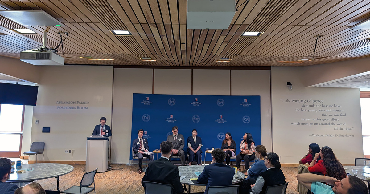 Five members of the second symposium panel on stage next to a speaker at a podium.