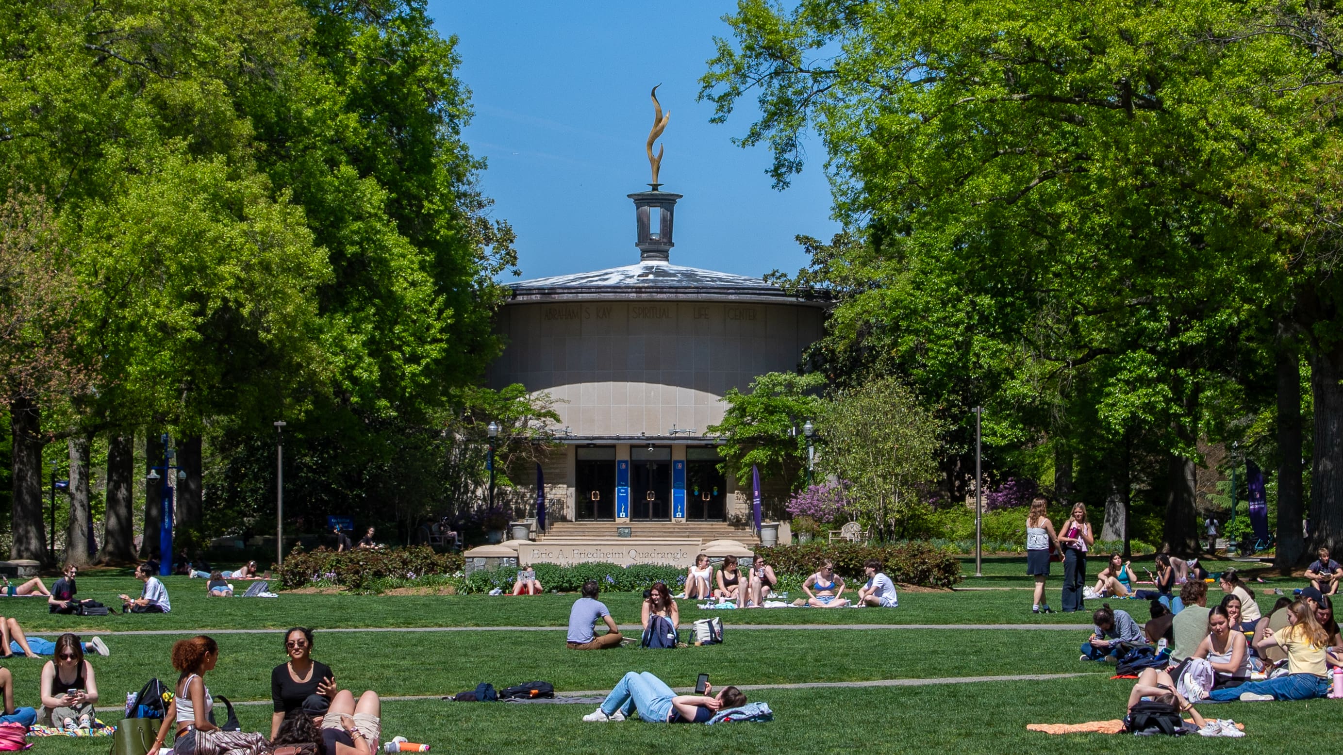 Kay Spiritual Life Center sits at the center of the image, blue sky above and students lounging on the Quad in front of it.