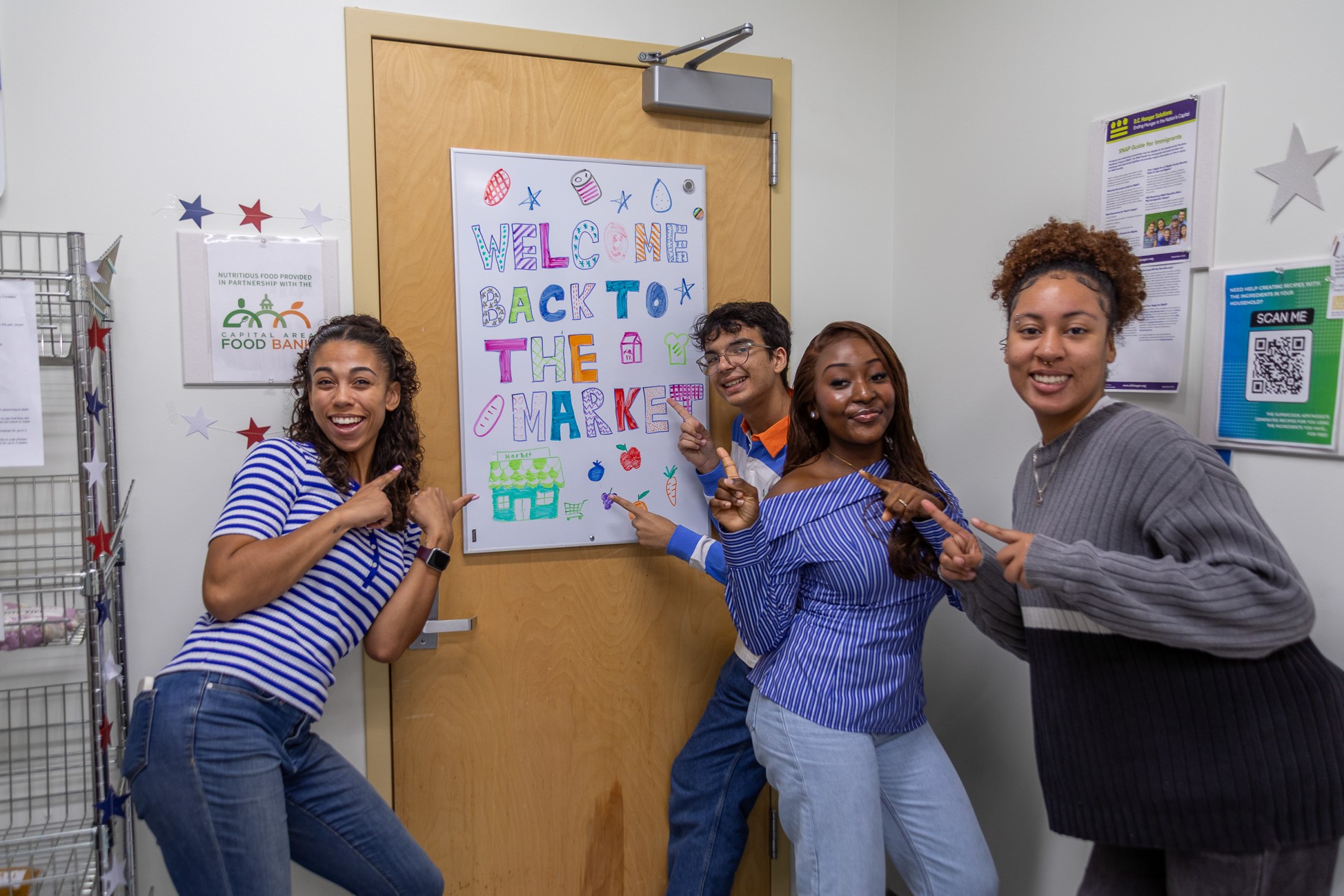 The Market staff stands by the front door, pointing to a sign that says Welcome to the Market.